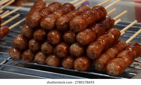 Close-up of a stack of grilled Thai fermented pork sausages (Sai Krok Isan) on skewers at a street food market.