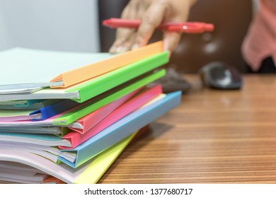 Close-up stack of homework assignment with plastic slide binding bars on table and teacher hand holding red pen for checking students score. Report papers stacks. Business and education concept.