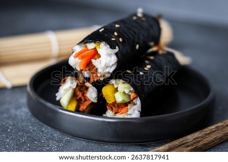 Close-up stack of mini Gimbap rolls, known as Mayak Gimbap. This dish has fresh ingredients like meat, carrot, cucumber, and pickled radish. An authentic Korean street food. Served on a black plate.