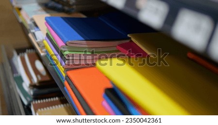 Close-up of stack of multicolored notebooks and exercise books on shelf in shop. Heap of composition books of solid vibrant colors lie for sale in store.