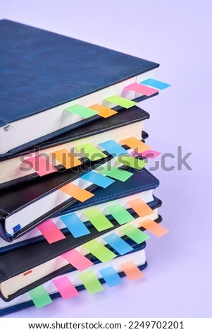 Close-up of a stack of office notepads with colorful sticky page markers sandwiched between pages on purple background