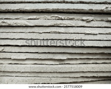 A close-up of a stack of plasterboards. The boards are covered in a layer of dust, and some have visible signs of wear and tear, such as chipped edges and scratches.