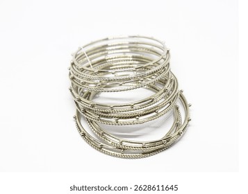 Close-up stack of shimmering silver colored metal bangle bracelets adorns white surface, exuding beauty and elegance with its intricate Indian design.