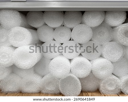 A close-up of stacked white bubble wrap rolls in a metal industrial shelf, providing essential cushioning for fragile items in shipping, storage, and packaging applications.