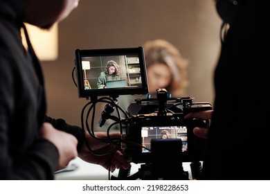 Close-up of steadicam screens with female model using laptop by table during commercial being shot by cameraman and his assistant