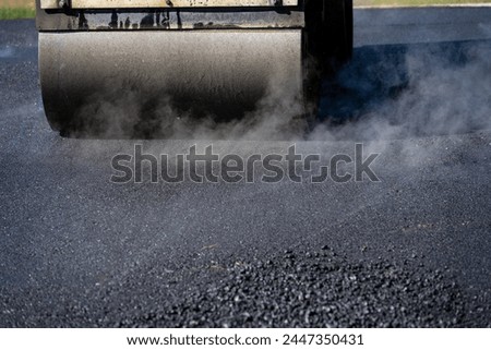 Closeup of a steamroller on freshly paved driveway to compact the hot asphalt, road construction project
