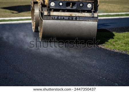 Closeup of a steamroller turning into a freshly paved driveway to compact the hot asphalt, road construction project
