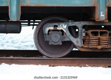 A closeup of a steel wheel of a train on the rail during a snowy winter. Rusty springs on the right side of the frame. Centered