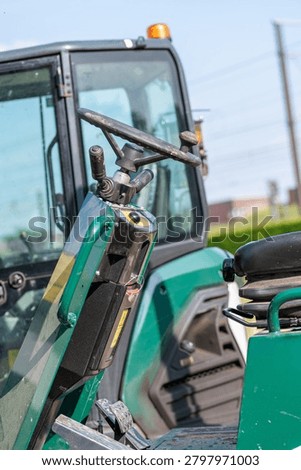 Close-up of a steering wheel and control column on a modern green utility vehicle or compact tractor. Operator's cabin details of industrial machinery with a steering wheel and adjustable steering column. Interior driver seat area of an open construction vehicle with mechanical control parts.
