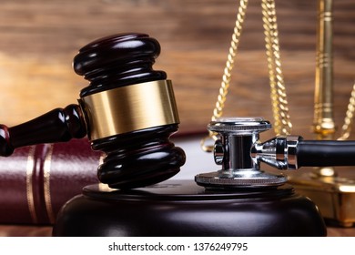 Close-up Of Stethoscope And Gavel In Front Justice Scale On Wooden Desk