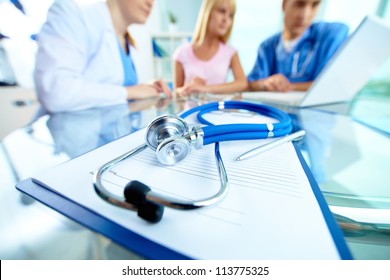 Close-up Of Stethoscope And Paper On Background Of Doctors And Patient Working With Laptop