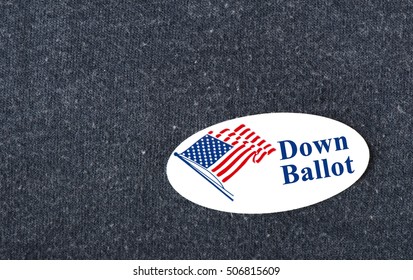 Closeup of a sticker with an American flag and the words "Down Ballot" placed on a navy shirt.