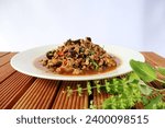 Close-up of stir-fried minced pork with holy basil with fresh shiitake mushrooms on a cream-colored porcelain plate on a trellis with leaves and basil flowers in front. white background

