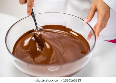 Closeup stirring mixing milk melted chocolate in glass bowl isolated on white background. Chocolatier make premium couverture hand-crafted chocolate. Candy making, pastry production, dessert concept