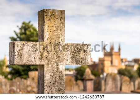 Closeup of a stone cross with the background of the cemetery of Guernsay.