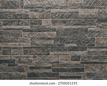 Close-up of a stone wall with rectangular tiles in varying shades of brown and gray. A geometric pattern is visible with a textured finish. Natural light highlights the intricate details.