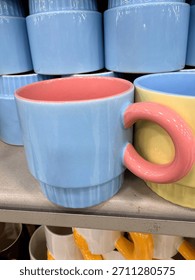 a close-up of a store shelf displaying a stackable ceramic mug with a light blue ribbed exterior and a bright pink interior, featuring a large, rounded pink handle.