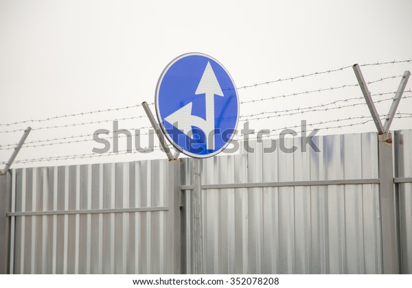 A closeup of straight and left turn\
arrow sign at the construction fence around\
airport