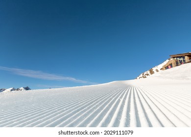 Close-up straight line rows of freshly prepared groomed ski slope piste with bright shining sun and clear blue sky background. Snowcapped mountain downhill landscape at europe winter skiing resort - Powered by Shutterstock