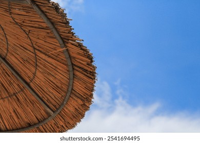 Close-Up of a Straw Beach Umbrella Under a Bright Sunny Sky: Summer Vibes and Coastal Relaxation - Powered by Shutterstock