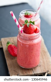 Closeup of strawberry fruit smoothies with strawberry pieces in glass with straw
