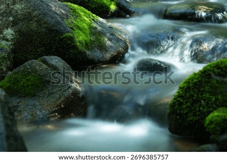 A closeup of a stream with a long exposure effect with  mossy,green stones around