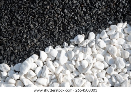 Close-up of a striking contrast between smooth white pebbles and dark black gravel, creating a visually appealing texture. Ideal for garden design, landscaping, or abstract nature backgrounds. 