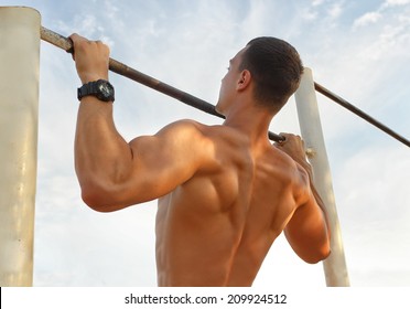 Closeup of strong  athlete doing pull-up on horizontal bar.Mans fitness with blue sky in the background and open space around him - Powered by Shutterstock