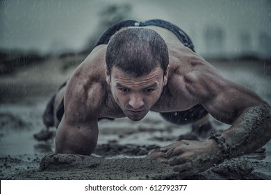 Closeup Of Strong Athletic Man Crawling In Wet Muddy Puddle In The Rain In An Extreme Competitive Sport 