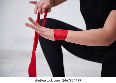 Close-up strong female boxer fighter preparing boxing bandages, wrapping her wrist and hands with a red tape, before wearing boxing gloves, getting ready for training, isolated over white background - Powered by Shutterstock