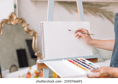 Closeup of student in apron painting in watercolor in an empty album on easel. Education, hobby, art concept. - Powered by Shutterstock