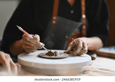 A Close-up of a student artist's hands focuses on sculpting clay with precision, using a tool to shape pottery piece. Learning process in an art studio, creativity, skill development, and dedication. - Powered by Shutterstock