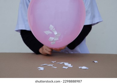 Closeup student do science experiment about static electricty from pink balloon and pieces of paper. Concept, Science project work activity. Learning by doing. Education.                            
