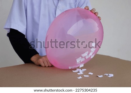 Closeup student do science experiment about static electricty from pink balloon and pieces of paper. Concept, Science project work activity. Learning by doing. Education.                         