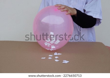 Closeup student do science experiment about static electricty from pink balloon and pieces of paper. Concept, Science project work activity. Learning by doing. Education.                              