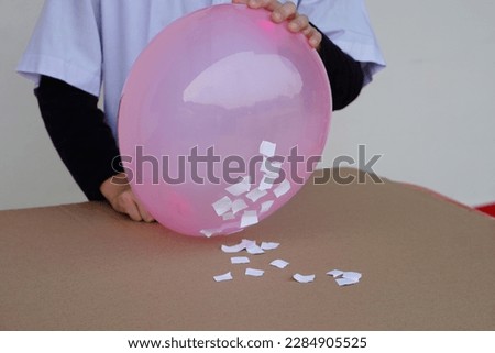 Closeup student do science experiment about static electricity from pink balloon and pieces of paper. Concept, Science project work activity. Learning by doing. Education.                             