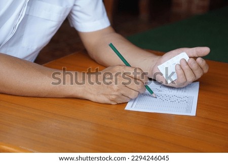 Closeup student doing examination, use pencil to write on paper and look at answers on another hand to cheat the test.  Concept, Dishonest behaviour. Education assessment.  