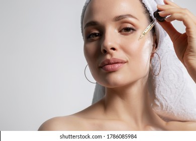 Nahaufnahme eines Studioporträts mit junger Frau in Badehandtuch auf dem Kopf einzeln auf Kopienraum mit Ölserum aus Pipette. Natürliches organisches Kosmetikprodukt für Gesichtspflege und Hautregeneration