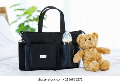 Closeup Studio Shot Of Black Color Multifunction Multipurpose Utility Newborn Toddler Accessories Handbag With Milk Baby Bottle In Elastic Pocket On Bed With Teddy Bear Doll