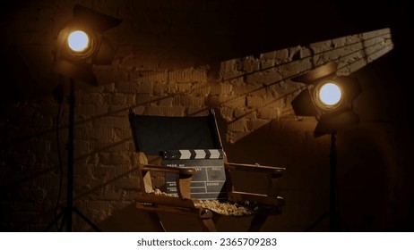 Closeup studio shot of clapperboard standing on director's chair, projectors at the background, popcorn scattered around.