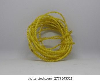 A close-up studio shot of a coiled bundle of bright yellow electrical wire against a plain grey background.