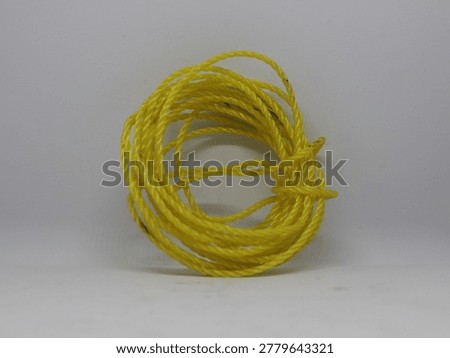 A close-up studio shot of a coiled bundle of bright yellow electrical wire against a plain grey background.