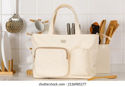 Closeup Studio Shot Of Cream Beige Color Large Multifunction Multipurpose Utility Newborn Baby Toddler Accessories Handbag With Stretching Pocket And Handle Placed On Kitchen Countertop With Utensils.