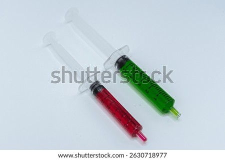 A close-up studio shot featuring two plastic syringes, one with red liquid and the other with green, highlighting their distinct colors and clear volumetric scales, suitable for illustrating concepts 