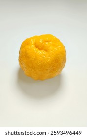 A close-up studio shot having a single, whole Summerina mandarin isolated on a plain white backround. The mandarin, characterized by its vibrant yellow-orange hue and textured, pebbly skin.