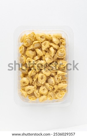 Close-up studio shot of an open plastic pack full of fresh Italian tortellini. Pack shot of transparent plastic box, top view shot, white background