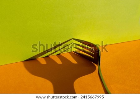 Closeup studio shot of the shadow of the tines of a fork on an orange and lime green background