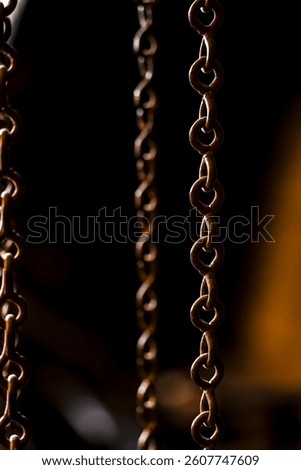 A close-up study of interlinked metal chains suspended in low light, revealing rusted edges and an industrial patina