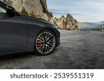 Close-up of a stylish car wheel and tire on a mountain road, highlighting sleek design and rugged surroundings. A blend of luxury and adventure