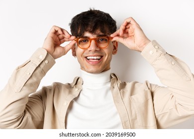 Close-up Of Stylish Hipster Guy Trying Eyewear At Optician Store, Put On Glasses And Smiling, Standing On White Background